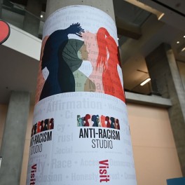 A concrete pillar wrapped with an ASH anti-racism studio poster.